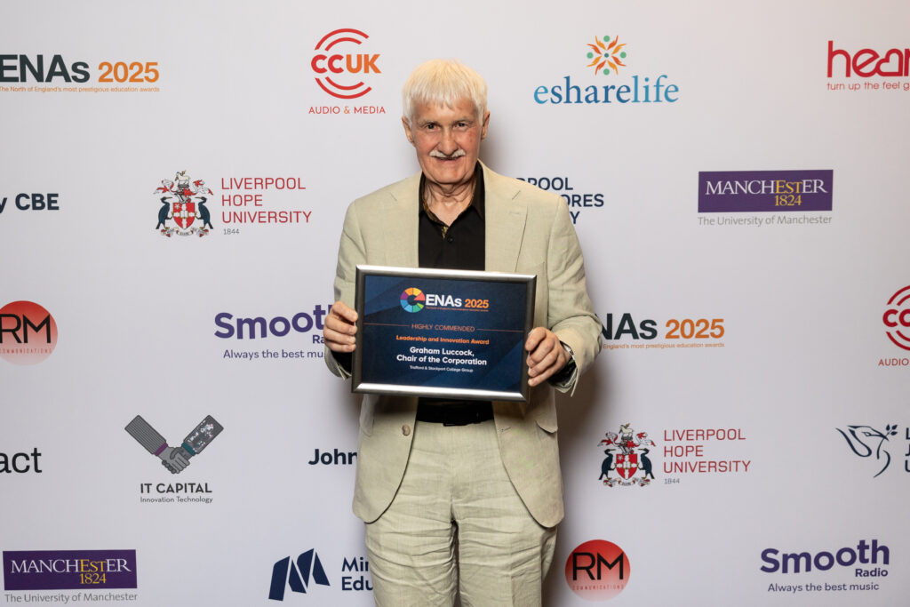Graham Luccock holding an ENAs 2025 award plaque in front of a sponsor-branded backdrop at an industry event.
