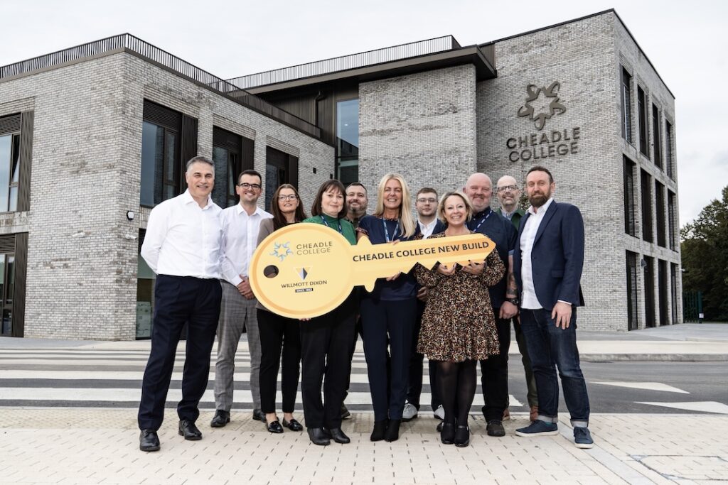 Group of project partners and college representatives standing outside the new Cheadle College campus, holding a large ceremonial key that reads “Cheadle College New Build.”